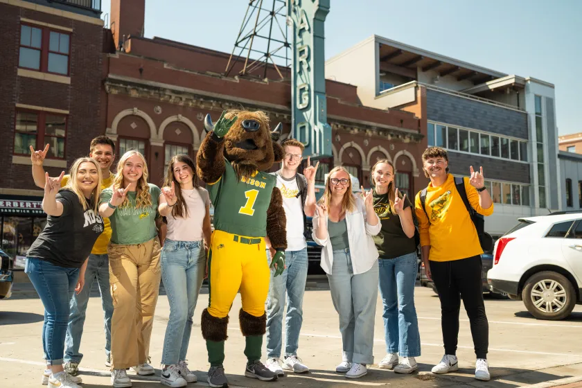 A group of NDSU students and mascot, Thundar, stand next to each other in front of the Fargo Theatre sign