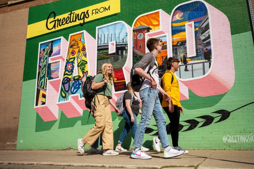 A group of NDSU students walk by a Greetings from Fargo mural