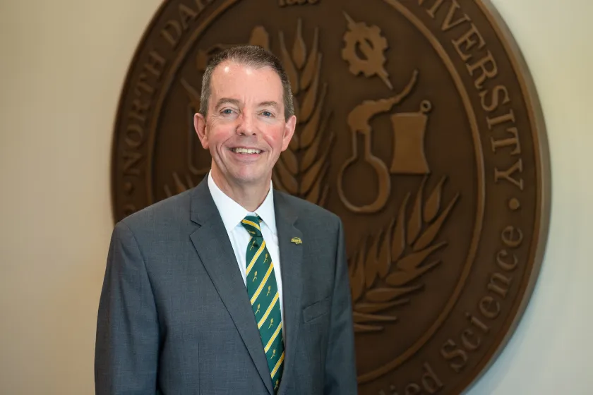 NDSU President Stewart poses in front of the NDSU Seal in Old Main