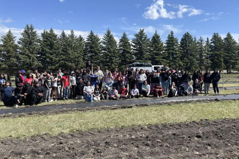 A group of students stand next to the trees they just planted in their school's orchard.