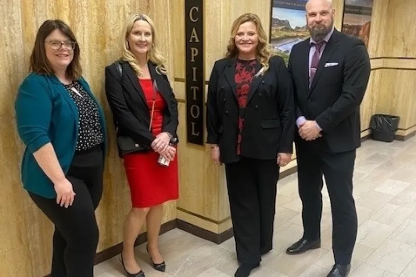 Four people dressed in business professional clothing stand side-by-site