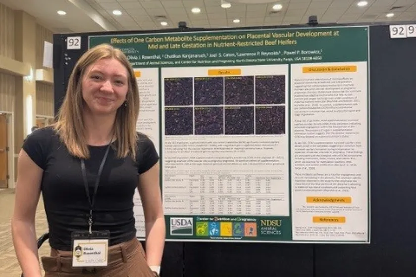 Undergraduate student stands next to her research poster.