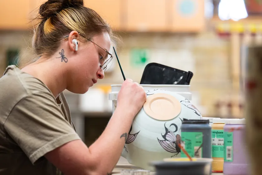 Student painting a clay pot
