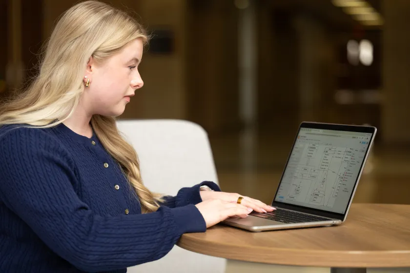 A woman sits at a table while looking at a laptop