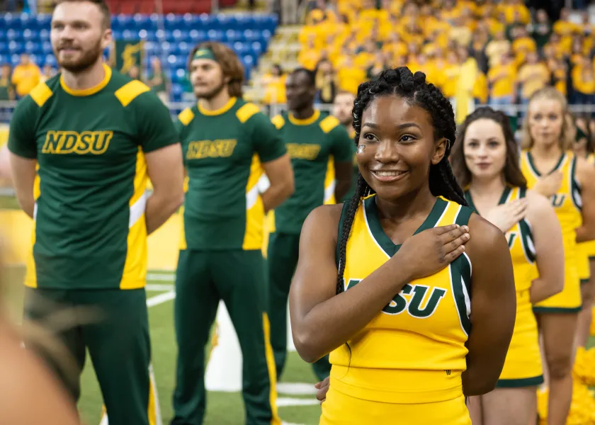 Cheerleaders standing with hand over their hearts. 