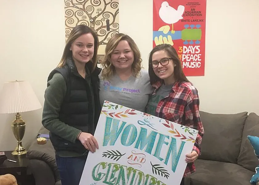 Three women holding a Women and Gender Studies sign while smiling confidently at the camera.