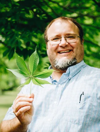 man smiling holding up a leaf from a tree