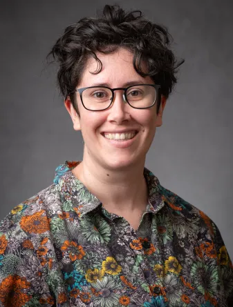 A headshot of Evelyn Milburn, a white woman with short brown hair and glasses. She is wearing a bright flowered collared shirt and smiling broadly.
