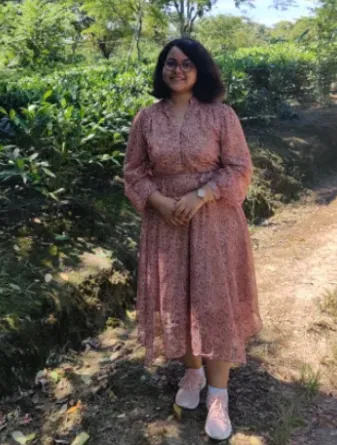Student standing in forested area smiling at camera.