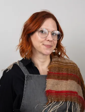 A women wearing overalls and a scarf draped over her shoulder smiling politely 