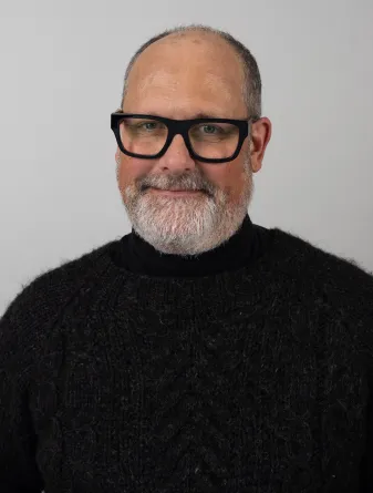 David Swenson wearing thick brimmed black glasses and a black sweater.