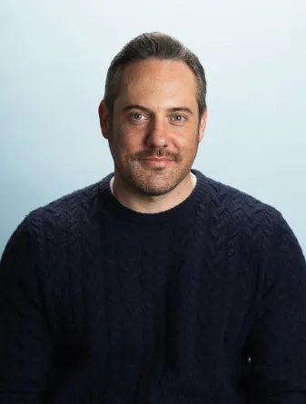 A man wearing a blue knit sweater looking confidently into the camera