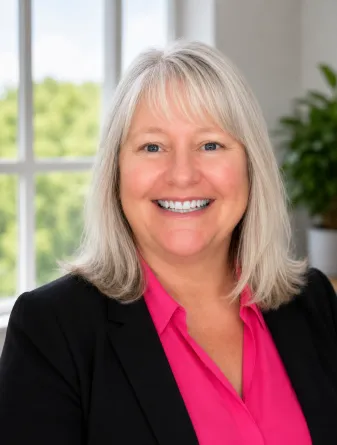 Laura is a caucasian female with light gray hair with blue eyes. She is wearing a hot pink shirt and black blazer. 