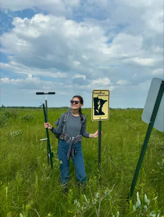 Josie Pickar standing in field holding equipment and sign.