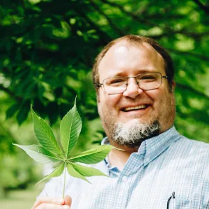 man smiling holding up a leaf from a tree