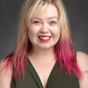 A women with long blond hair with pink ends. Wearing red lipstick and a green shirt