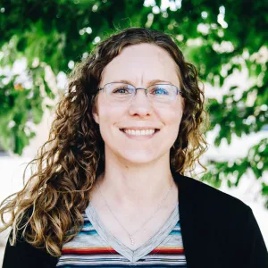 A woman stands smiling in front of a tree