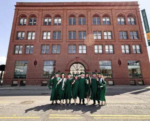 Students in cap and gown in front of downtown NDSU building