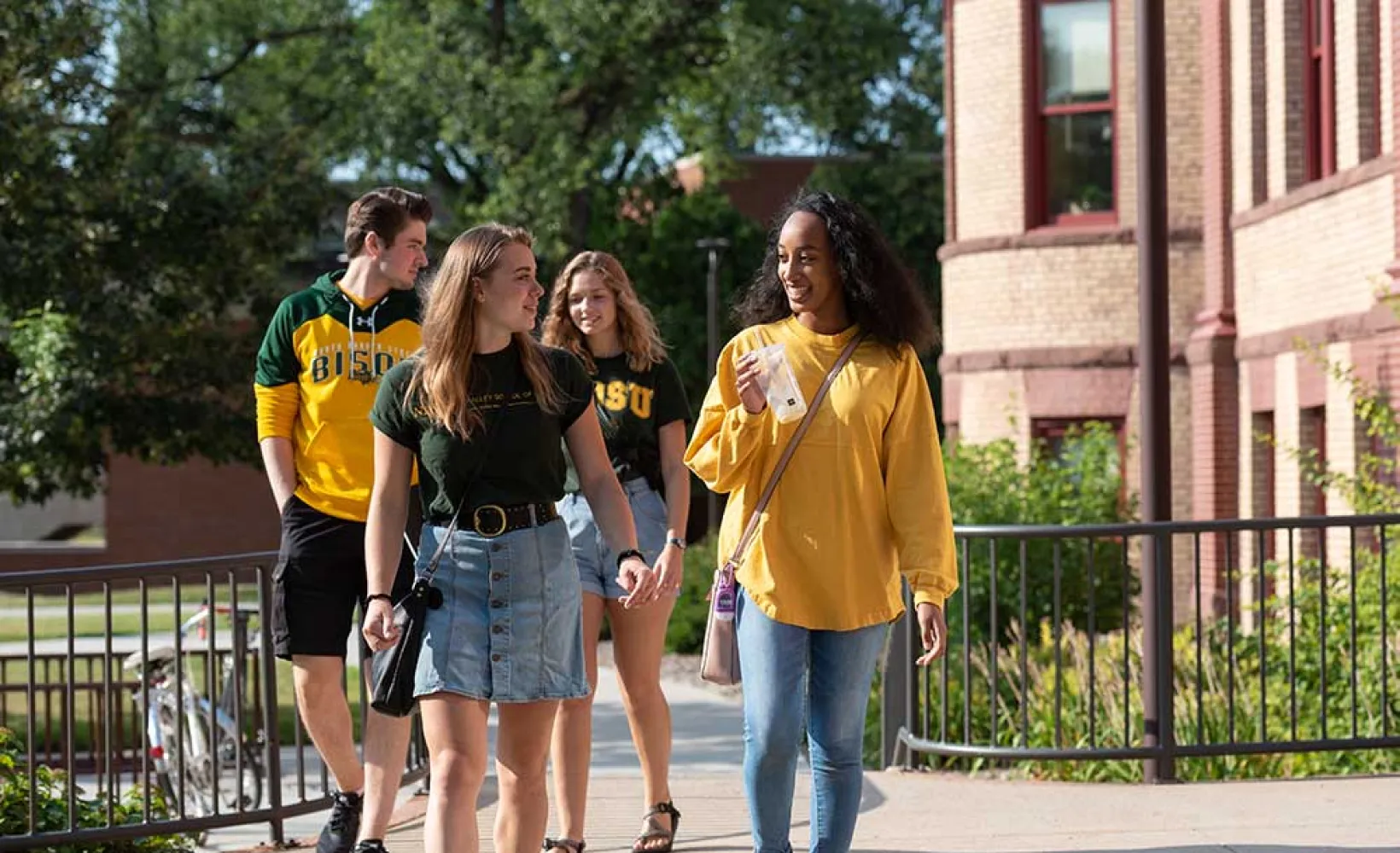 "Four students walking on sunny day."
