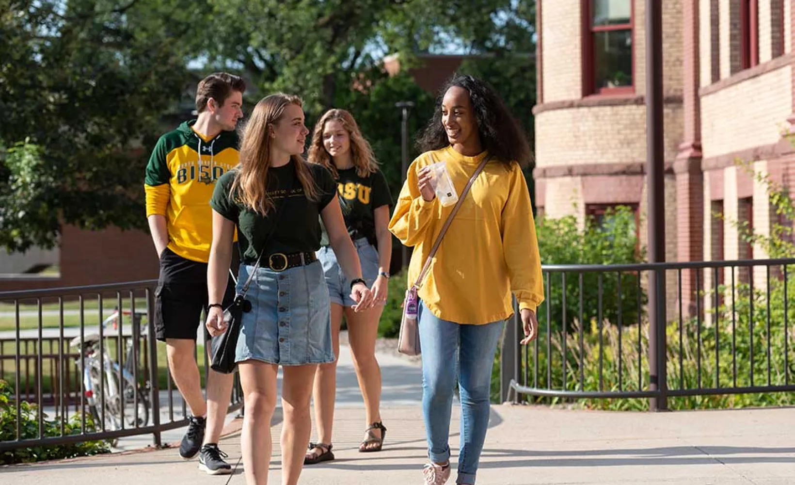 "Four students walking on sunny day."