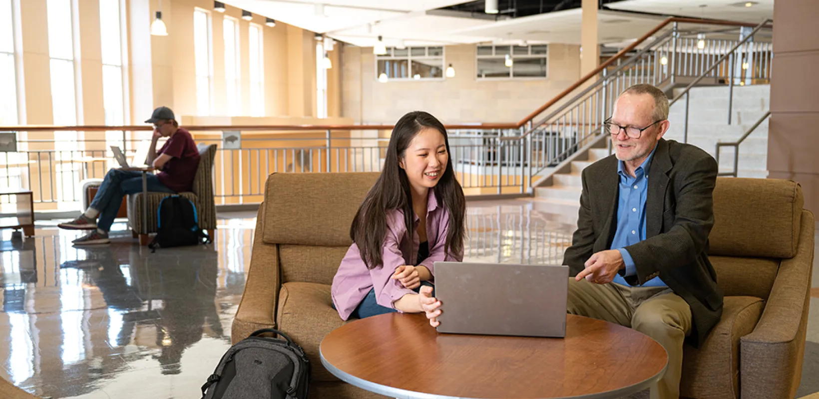 Student showing work to instructor on laptop in Barry Hall study area.