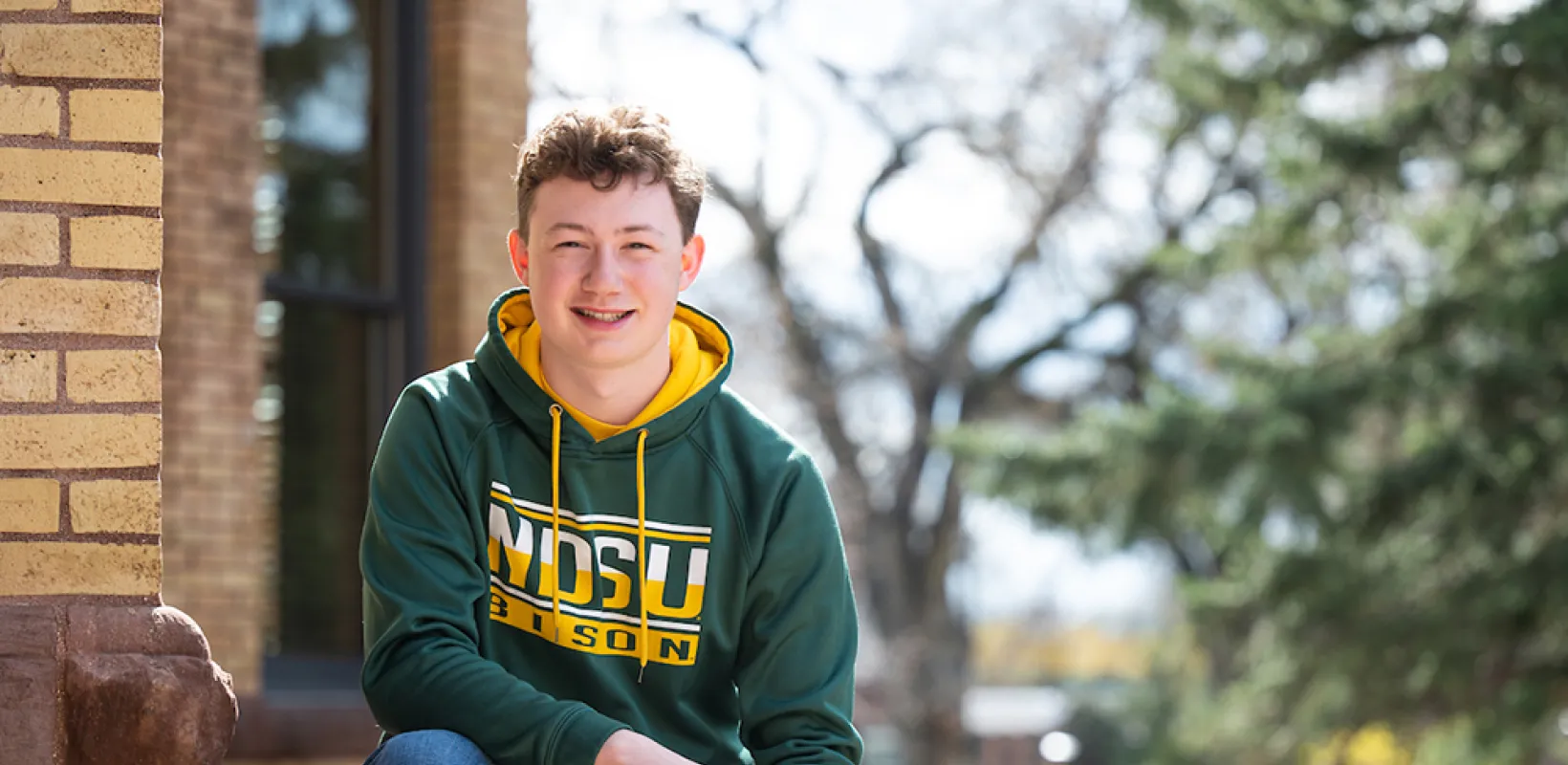 Rylan Swenson sitting in front of a building on campus