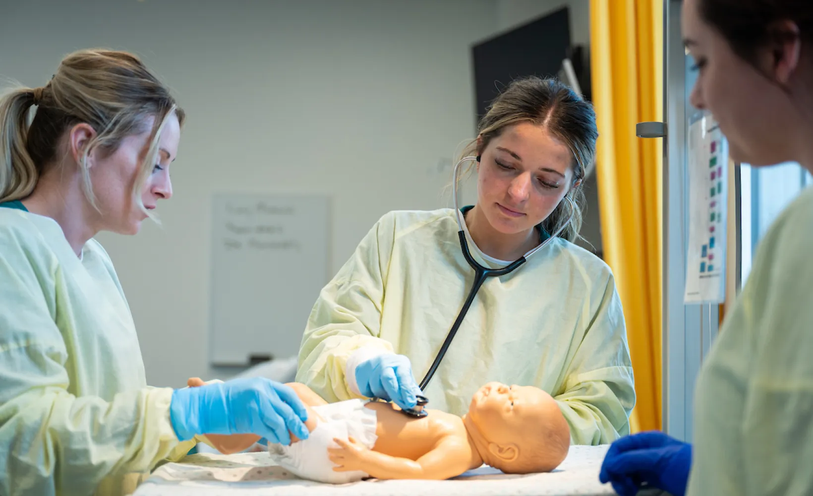 nursing students practicing infant patient care using a mannequin