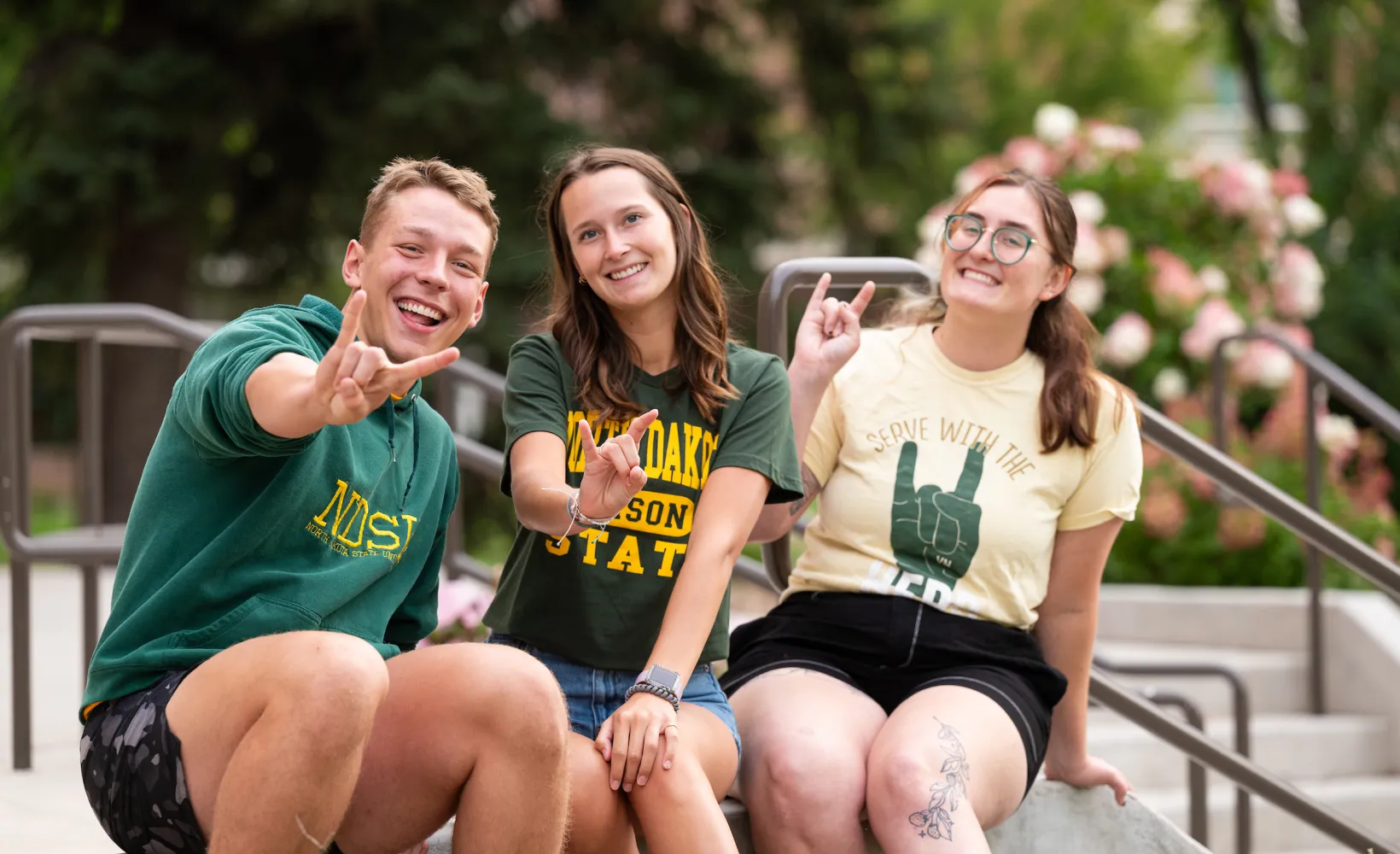 Three students giving 'horns up' on steps
