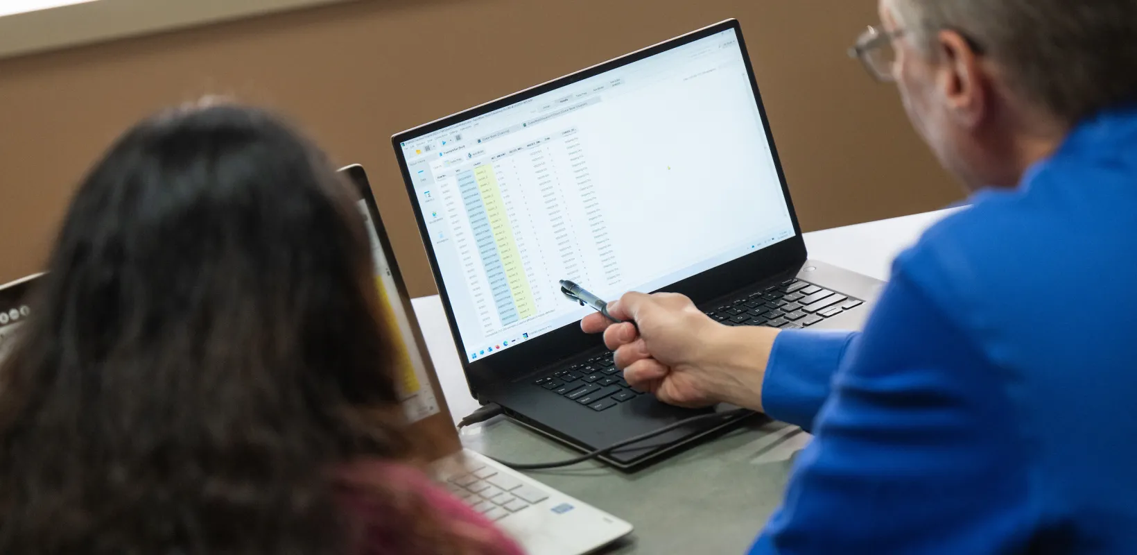 professor helping a student with a spreadsheet on a laptop