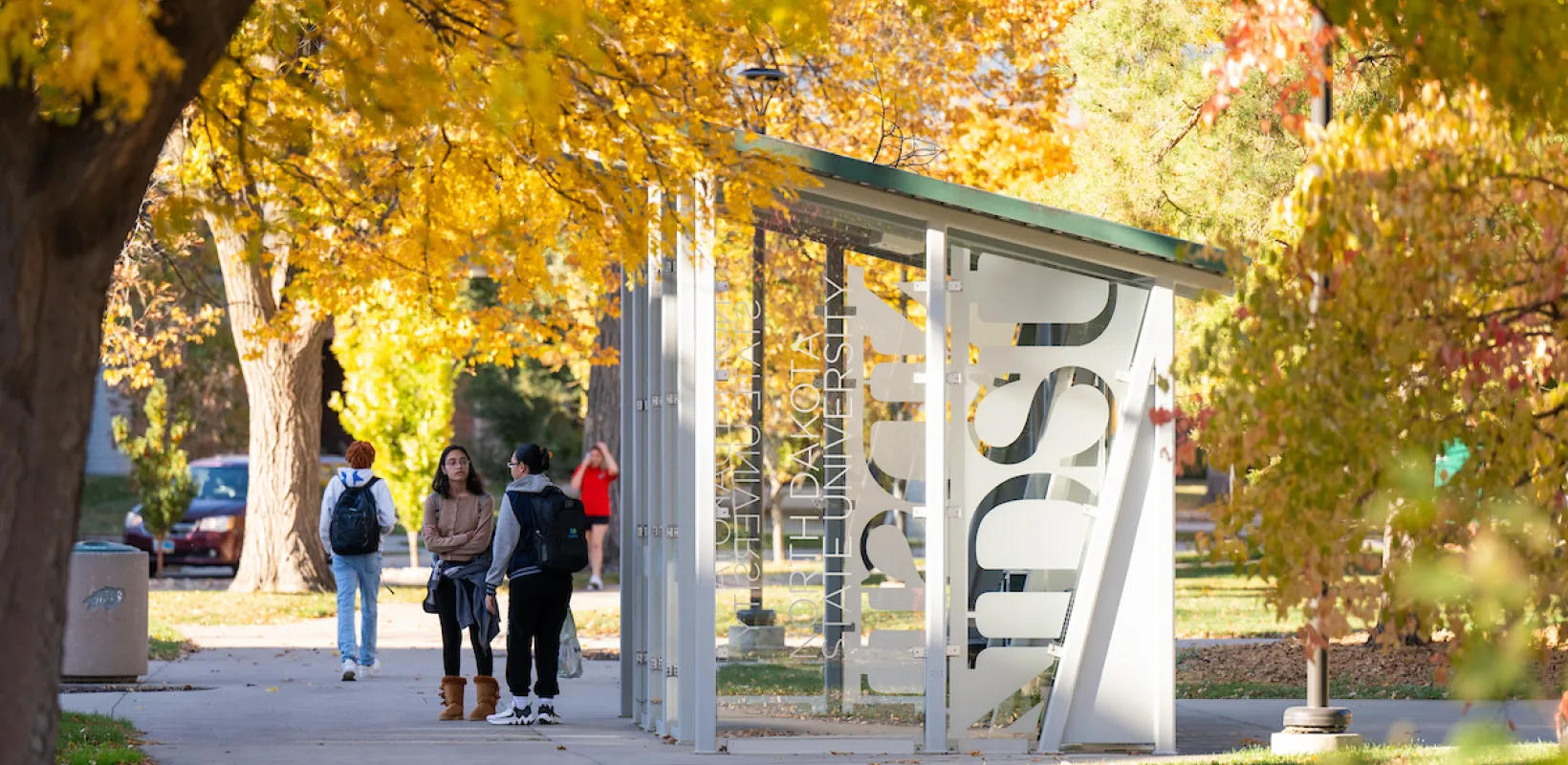 students waiting by bus shelter on campus on a fall day