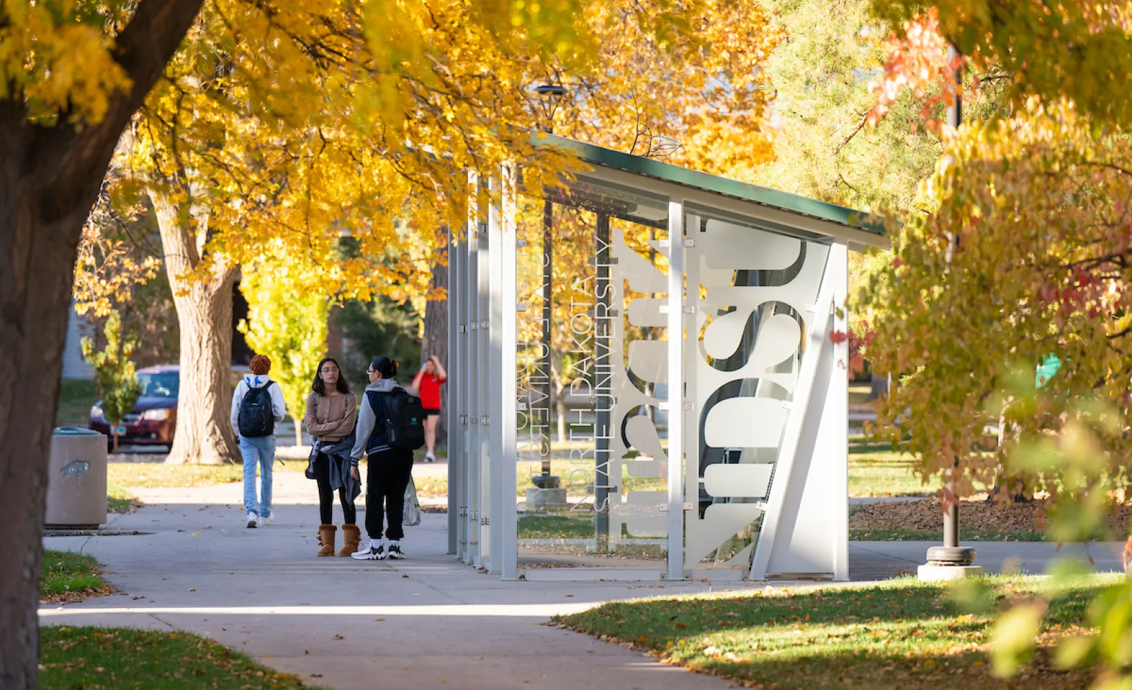students waiting by bus shelter on campus on a fall day