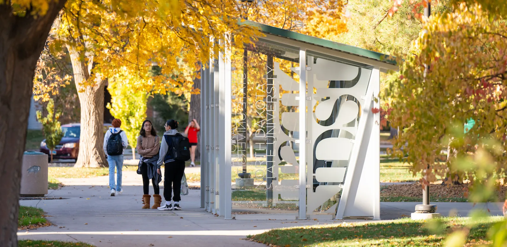 students waiting by bus shelter on campus on a fall day
