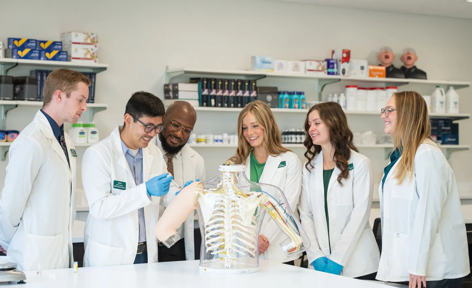 Pharmacy students in a lab observing a student administering a shot to a dummy arm