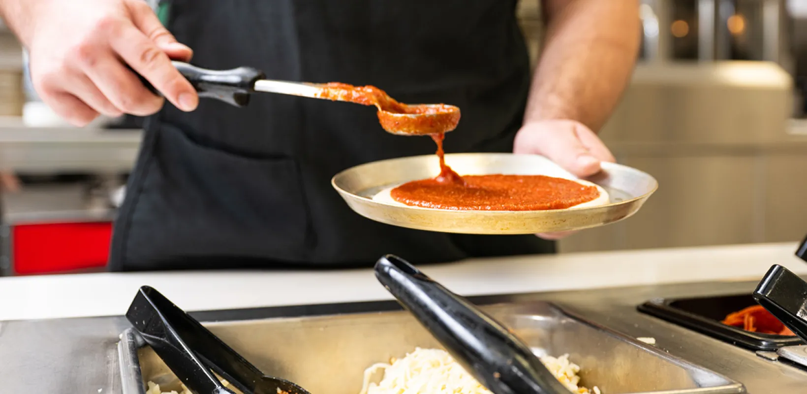 A team member spreading sauce on a pizza at the dining center