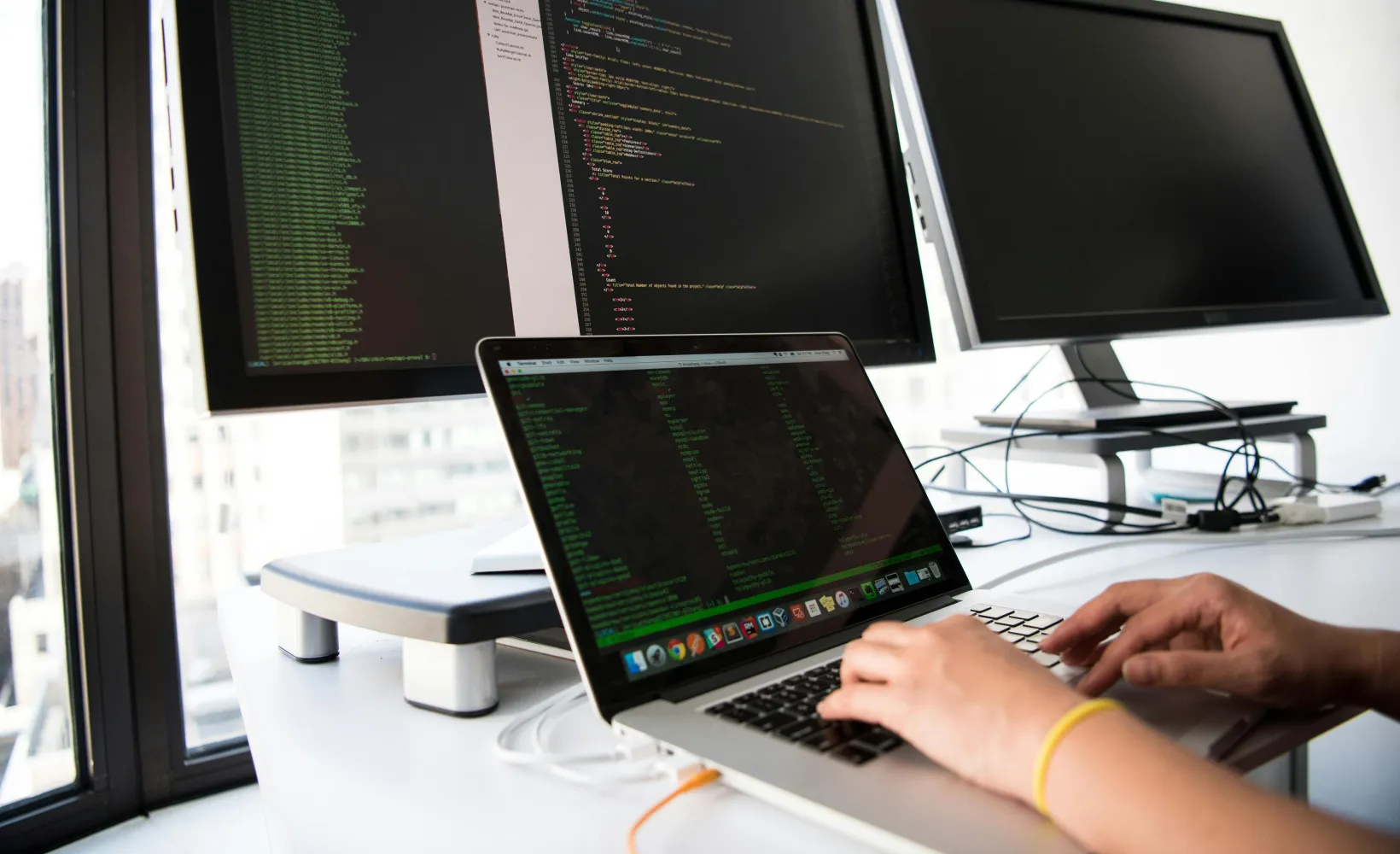 close up of hands on a laptop keyboard with multiple computer monitors in the background
