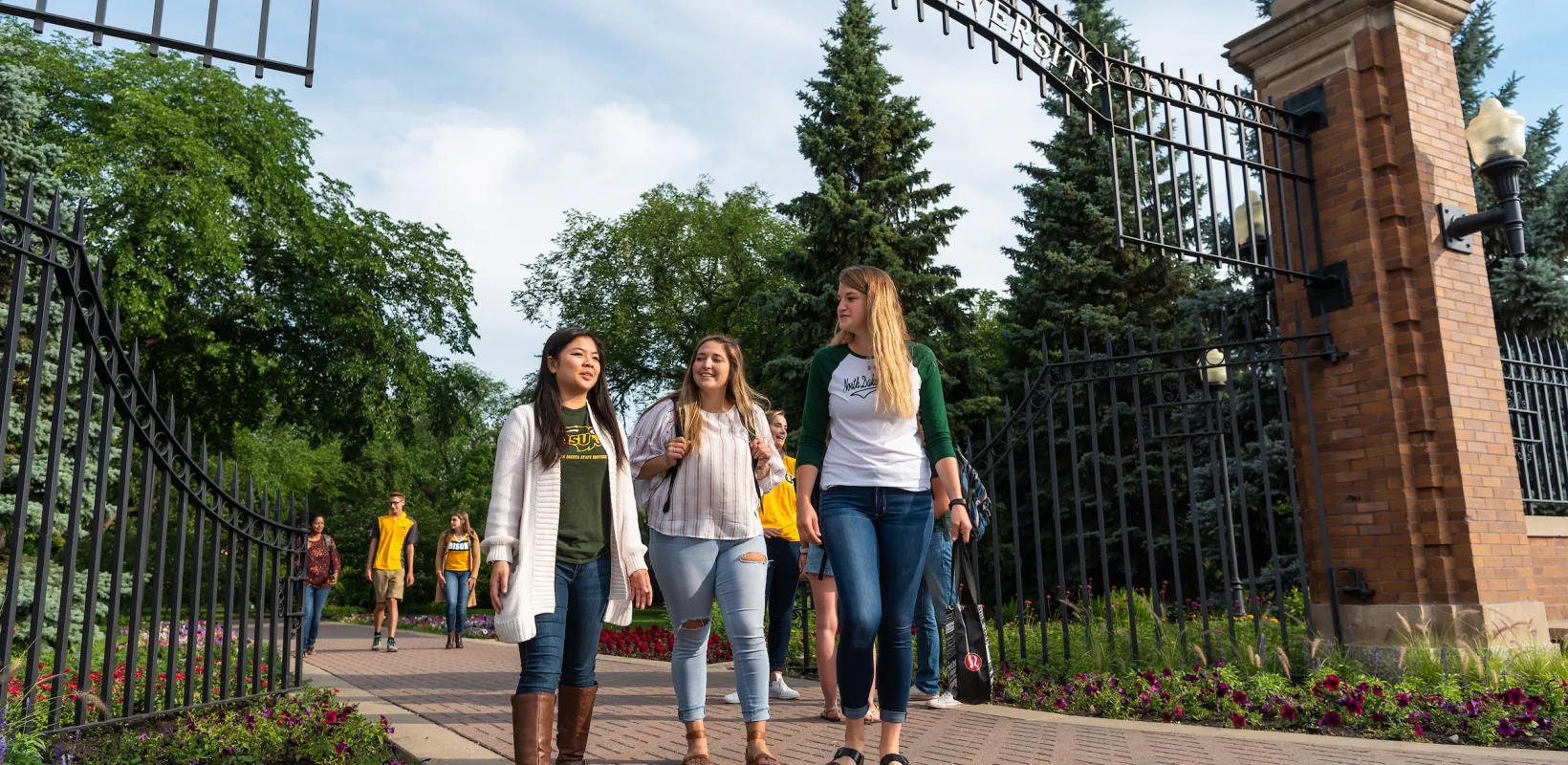 Three students walking through the NDSU gate, all wearing green and gold attire.