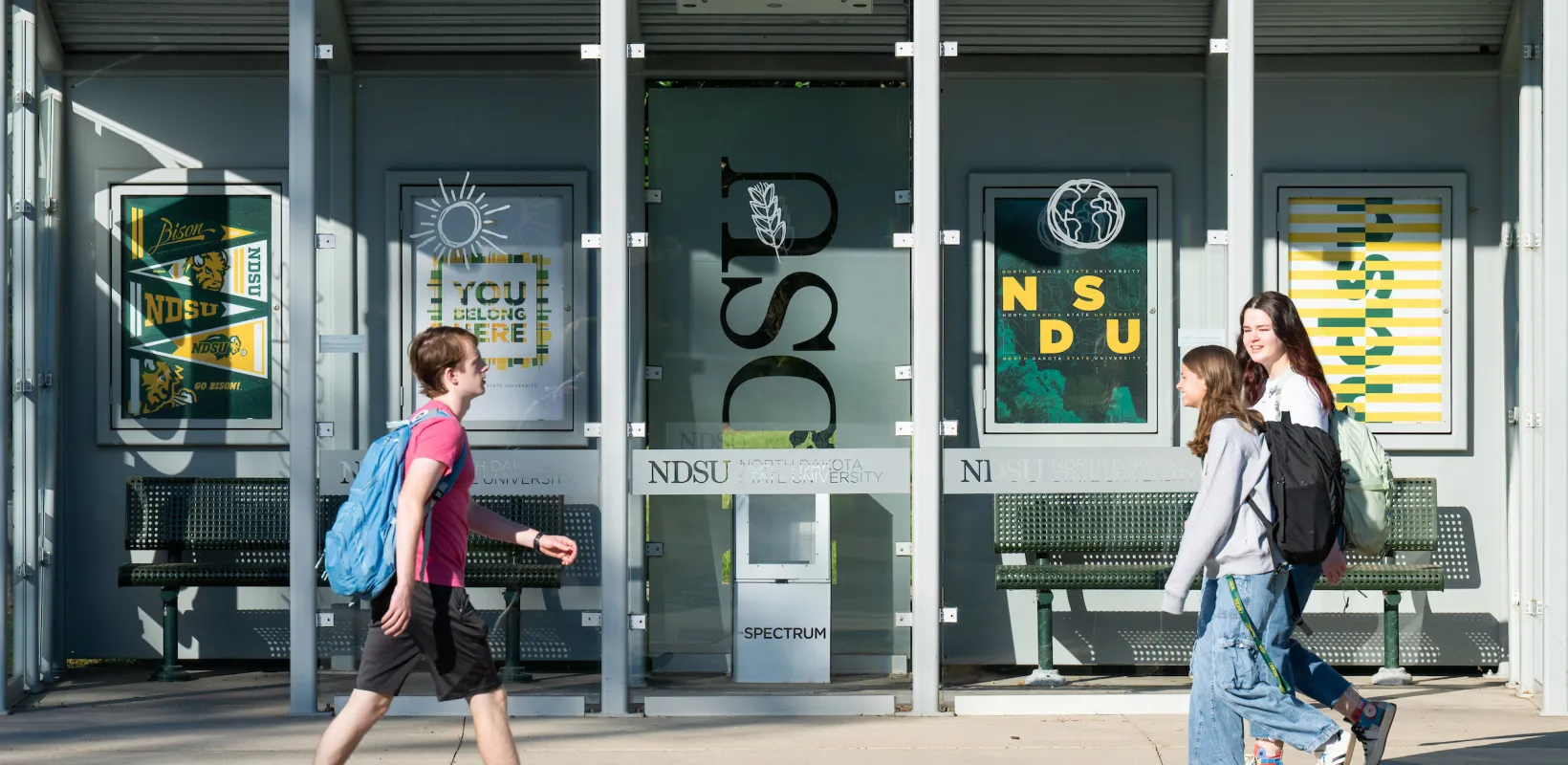 three students walking in front of bus stop on campus