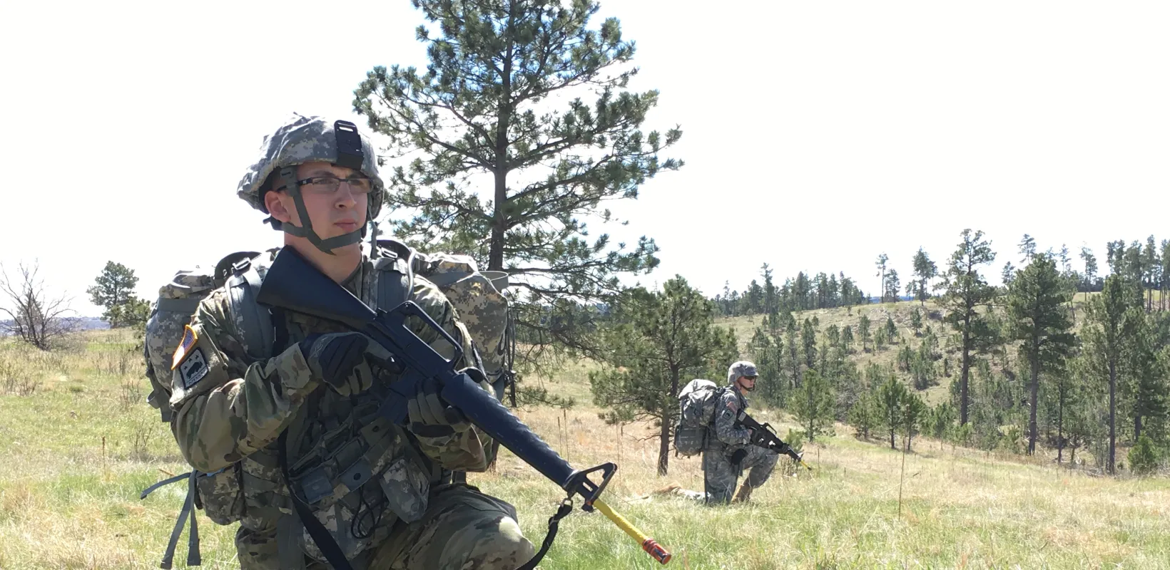Army ROTC Cadet in full combat gear with weapon practicing Military movements in wooded area.