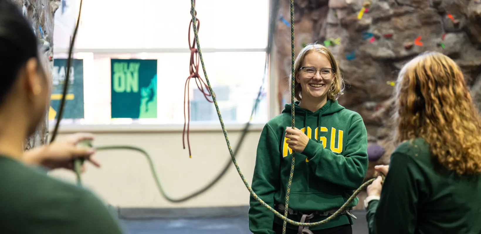 Student in green NDSU student instructing others on climbing techniques at Wellness Center Climbing Wall