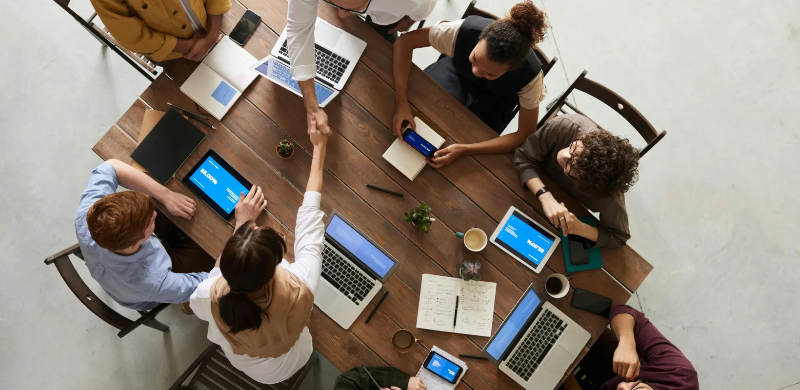 birds eye view of working professionals with laptops sitting at a table and shaking hands