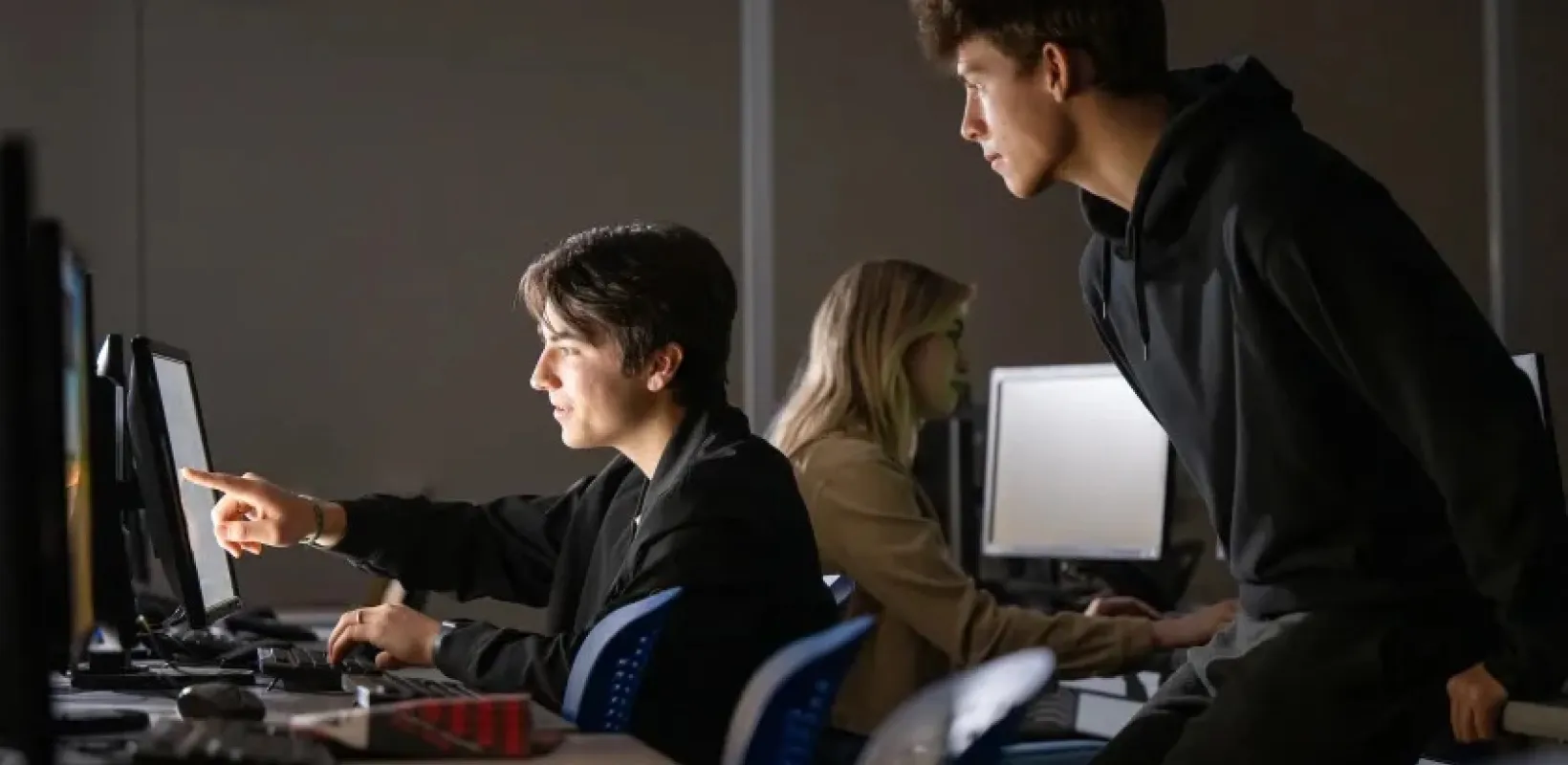 students in a dark computer lab looking at a computer monitor