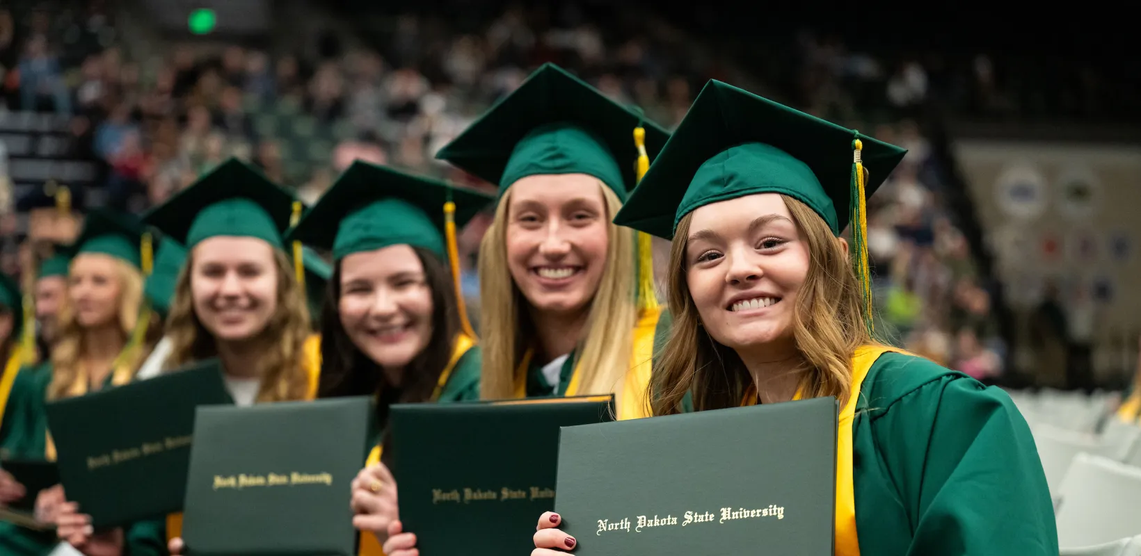 group of smiling students during commencement ceremony holding their diplomas