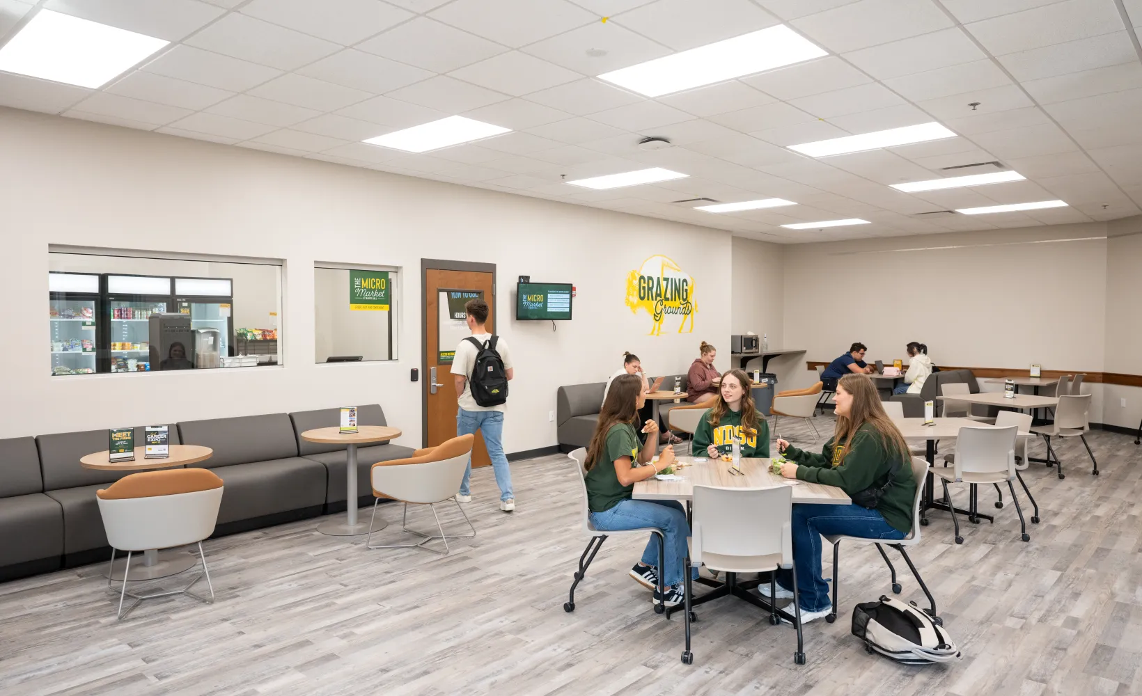 Outside shot of the Micro Market where three groups of students sit at tables talking and studying at Barry Hall