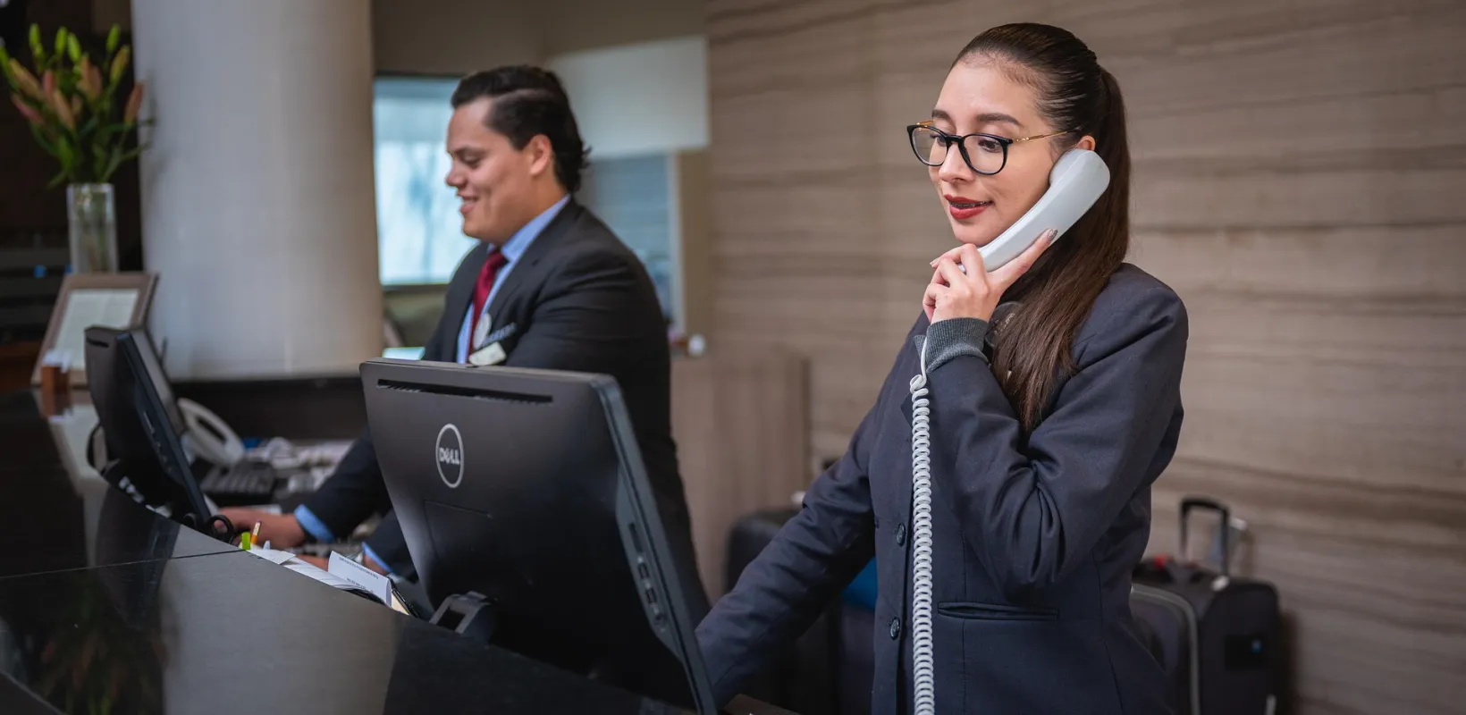 Two Hotel front desk clerks, one on phone providing customer service