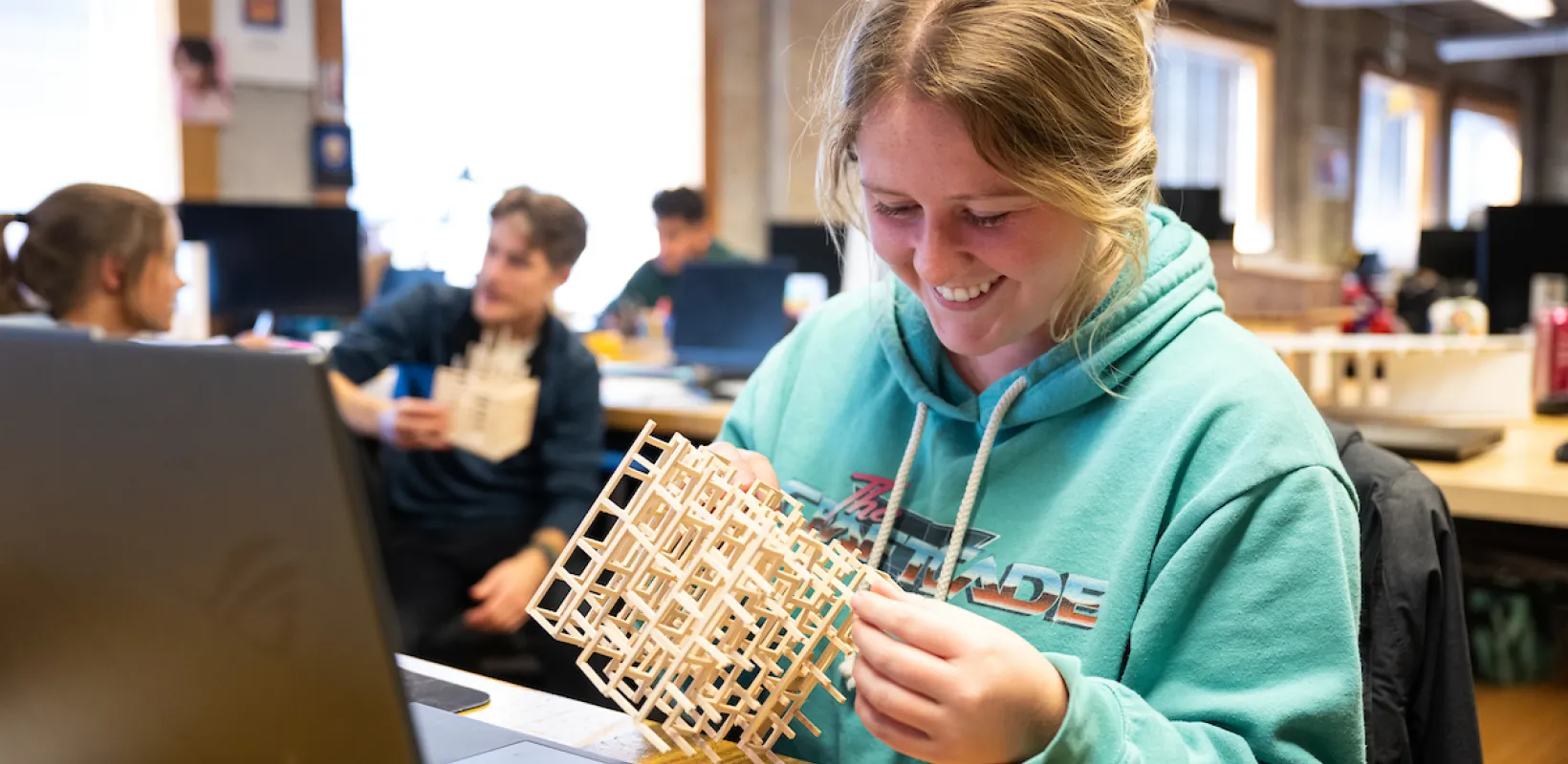 Student working with a wooden model while sitting in front of her computer.