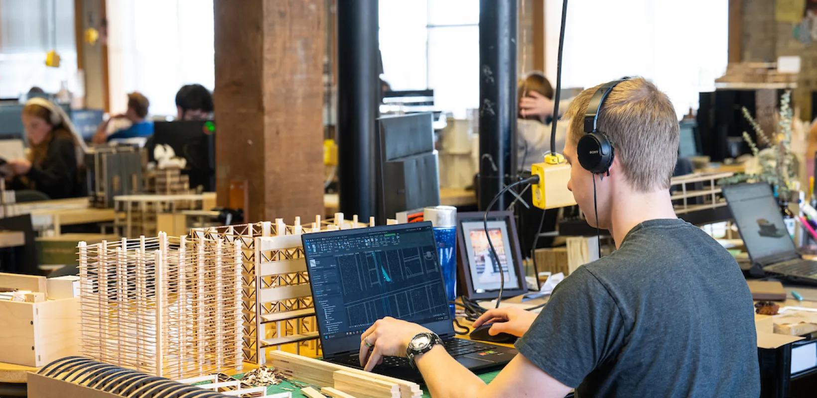 Architecture student working at computer with building models surrounding the desktop.