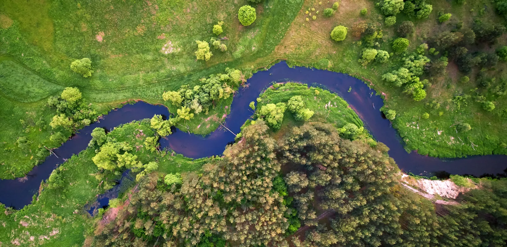 An aerial photo of a river winding through a green fields and trees