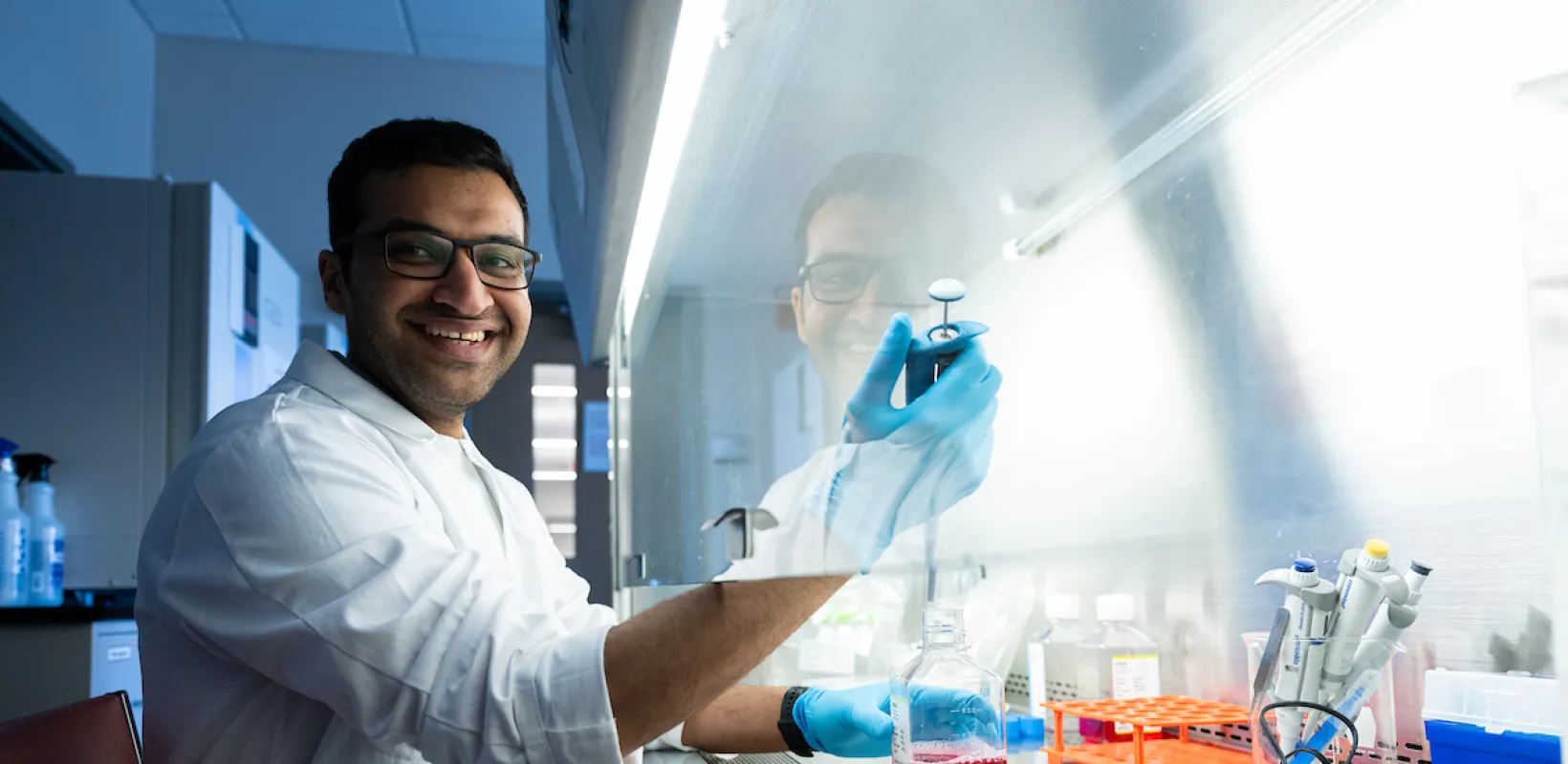 Research student in lab wearing a white coat smiling confidently at camera.