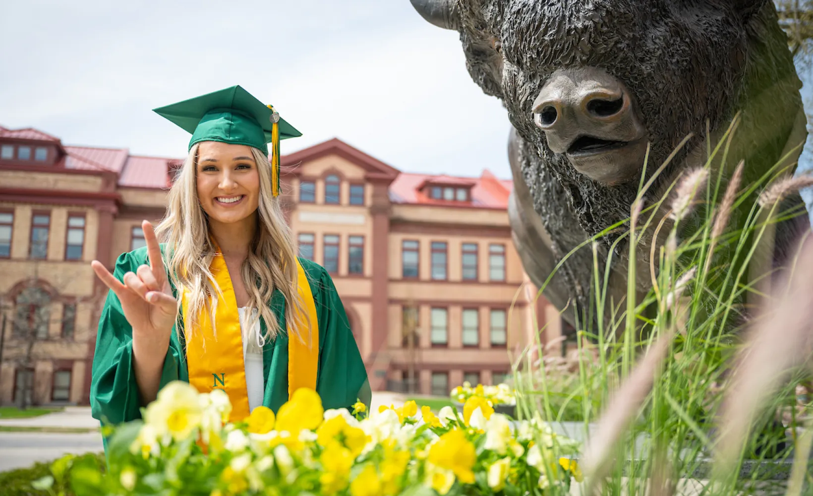 graduate giving bison horns next to bison statue