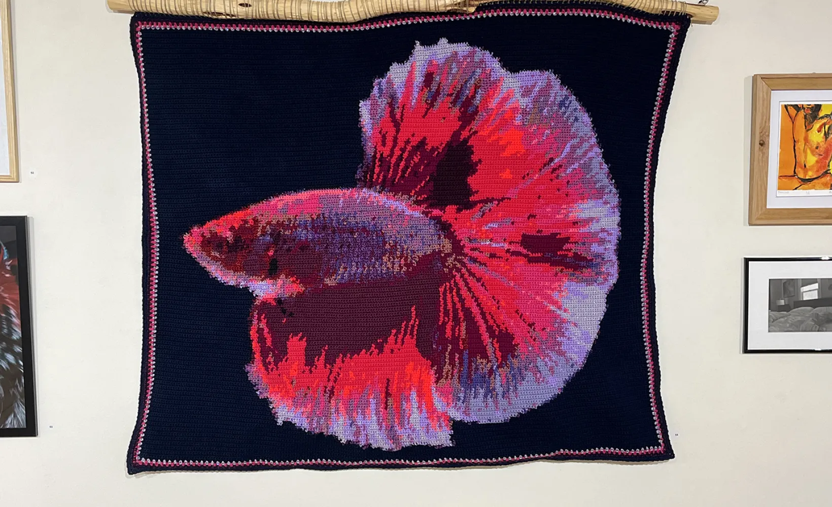 a Woven image of a colorful beta fish is hung on the wall beside other artworks